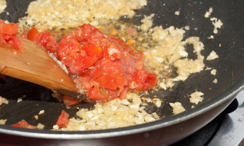 1. Этап. Жареные куриные ножки на сковороде: За десять минут до окончание мариновки, в сковороду с высокими бортами налейте растительного масла. Выложите мелко рубленный лук. Обжарьте его. Когда лук станет мягким, добавьте, нарезанные на маленькие кубики, помидоры.