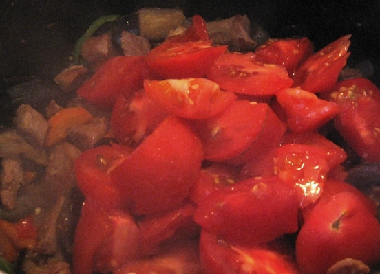 1. Этап. Баклажаны, жаренные со свининой: Моем помидоры, нарезаем дольками и через 5 минут после того, как бросили перец, добавляем к мясу с баклажанами.