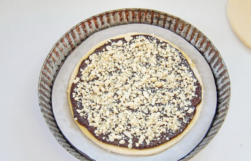 1. Этап. Слоеный шоколадный пирог: 5. Возьмите первый слой теста и положите его на противень или в любую подходящую форму для выпечки, застелив дно пергаментом. Смажьте сверху тесто обильно начинкой и посыпьте орехами, немного оставьте орехов для верха.