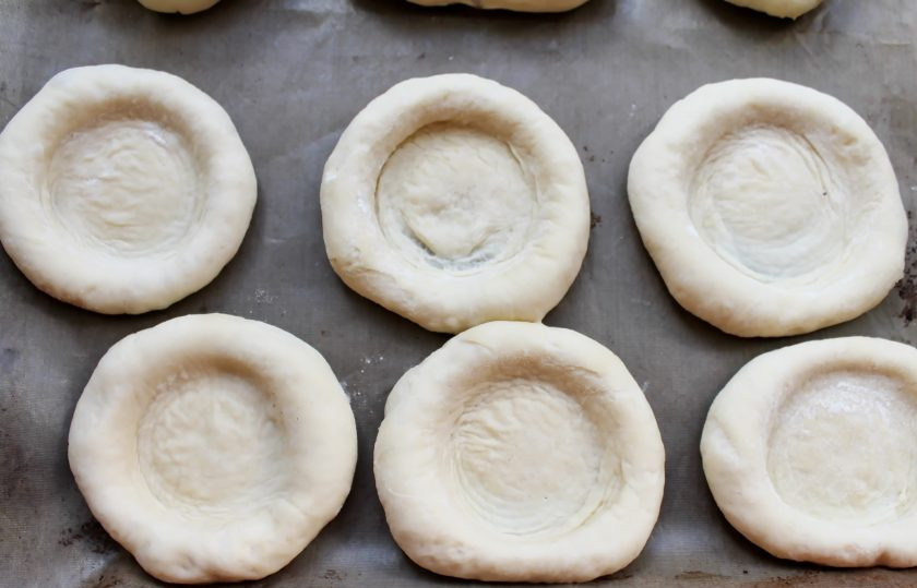 1. Этап. Ватрушки с черникой: При помощи обычного стакана сделайте углубления в шариках теста.