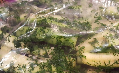 1. Этап. Огурчики в мешочке: Возьмите прочный прозрачный мешок. Он должен быть обязательно целым, без единой дырочки, иначе сок, выделяемый огурцами, будет вытекать. Положите в мешочек огурцы с зеленью и чесноком, посолите. Хорошенько потрясите и оставьте на сутки мариноваться в холодильнике. При подаче можете заправить огурчики малом.