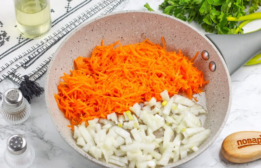 1. Этап. Замороженные голубцы на сковороде: Нарежьте луковицу мелкими кубиками, а морковь натрите на терке с мелкими ячейками. Прогрейте растительное масло в сковороде и выложите в емкость все нарезки. Обжарьте в течение 3-4 минут до румяности.