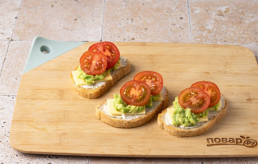 1. Этап. Бутерброды с авокадо, сыром и помидором: Сверху выложите помидоры черри. В конце добавьте пару листиков рукколы, посолите и поперчите помидоры.