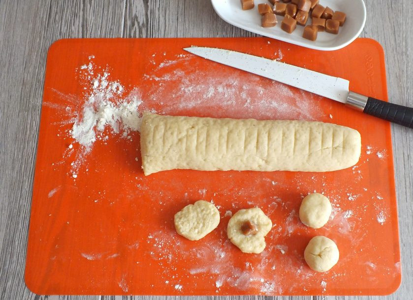 1. Этап. Печенье с ирисками: Разрежьте тесто на 22 части. Каждую часть подкатайте в шарик, расплющите в лепешечку и выложите половинку ириски. Скрепите тесто, придайте печенью вид шарика.