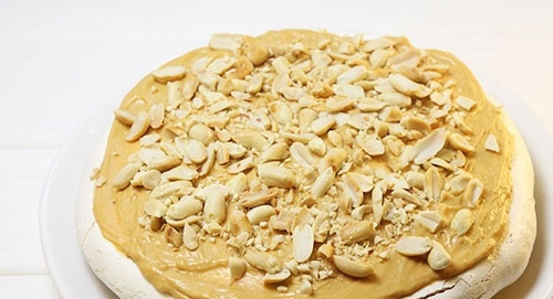 1. Этап. Торт Сникерс с безе: 17. Сверху выложите безе, смажьте кремом и снова присыпьте орешками.