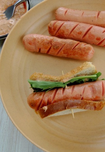 1. Этап. Хот-дог с хлебом: Выложить в центр сосиску и пару листиков зелени можно вложить зелень и после подсушивания хот-догов, так она не повянет и сохранит свой вид). Закрепить по центру зубочисткой.