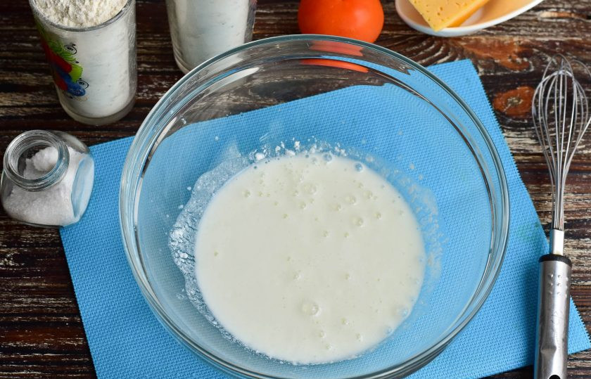 1. Этап. Заливной пирог с помидорами и сыром: В миску влейте теплую простоквашу, всыпьте соль и соду. Перемешайте.