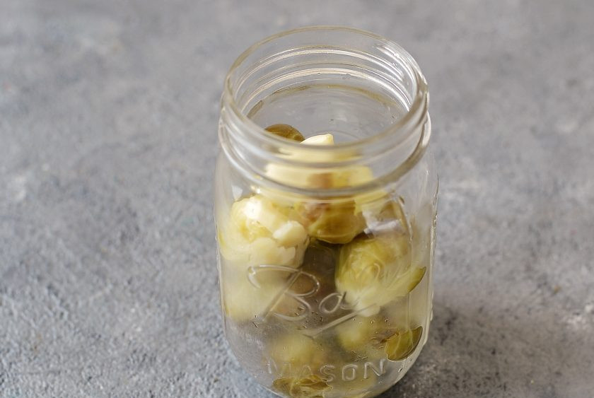 1. Этап. Брюссельская капуста на зиму: Разложите капусту по чистым стерилизованным банкам, добавьте зубчики очищенного чеснока.