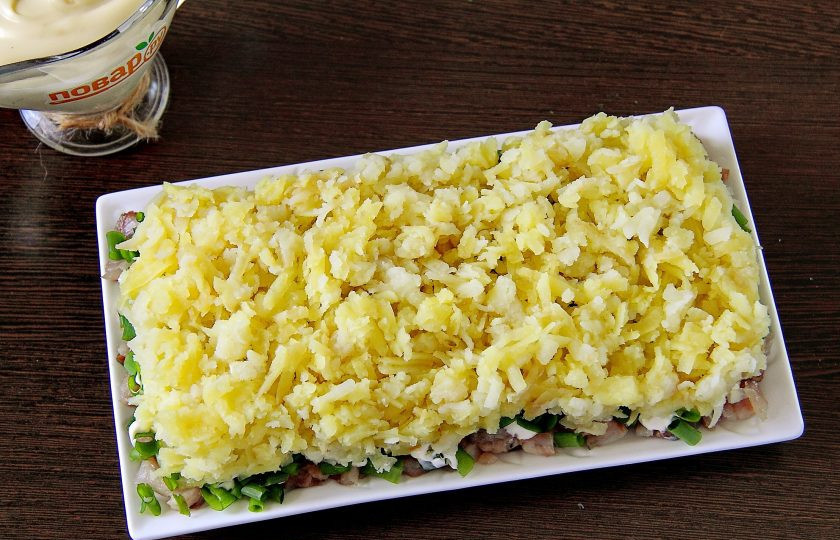 1. Этап. Салат Зеленая шуба: Далее идет слой тертого картофеля. Картофель по желанию можно немного посолить по вкусу, после чего смазать майонезом.