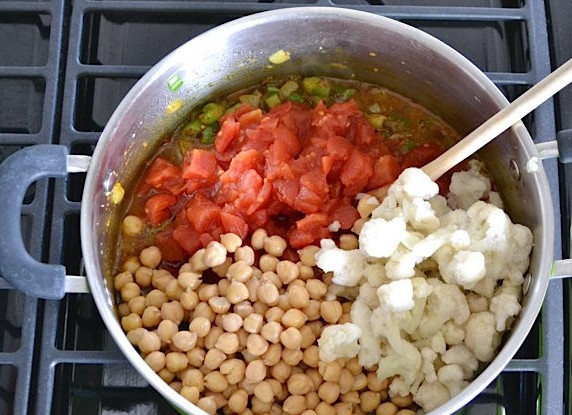 1. Этап. Овощное рагу без мяса: Нарежьте консервированные томаты, отправьте в сотейник к луку вместе с жидкостью, туда же отправьте нут, капусту, разделенную на соцветия.