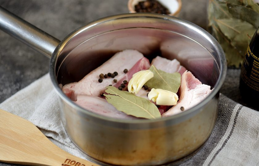 1. Этап. Сало в соевом соусе: Всыпьте щепотку перца горошком, добавьте лавровый лист и раздавленные тыльной стороной два крупных зубчика чеснока.