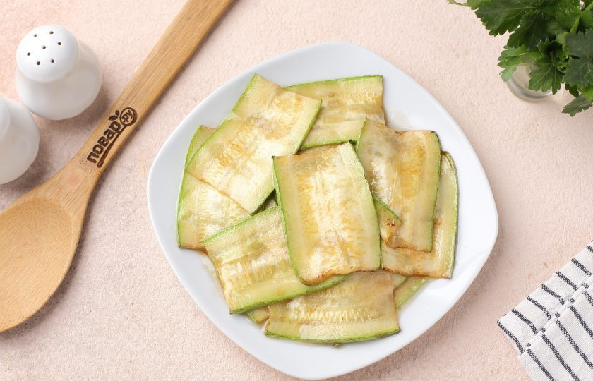 1. Этап. Пирог из лаваша с фаршем и кабачком: Нарежьте кабачок на продольные полоски, толщиной около 5 мм. Я каждую полоску ещё разрезала на две части, но если кабачок не сильно длинный, то можно этого не делать. В сковороде разогрейте масло, выложите кабачки и обжарьте с каждой стороны буквально по 1-2 минуты. Сильно зажаривать кабачки не нужно, самое главное — это сделать их мягче.