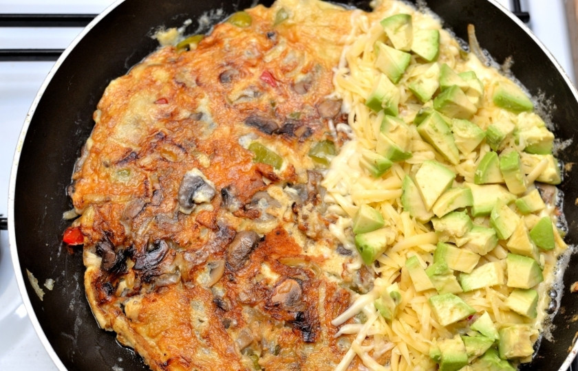 1. Этап. Омлет с сыром и овощами: Почистите авокадо, нарежьте маленькими кусочками и положите поверх сыра.