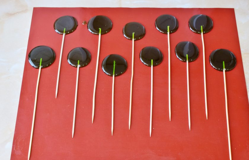 1. Этап. Домашние леденцы без формочек: На столе разложите силиконовый коврик. Ложкой выливайте на него карамель в виде леденцов. Шпажку вставьте снизу в леденец и слегка прокрутите. Оставьте леденцы на столе до полного остывания.