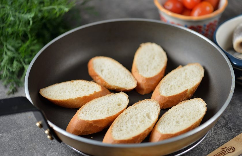 1. Этап. Канапе с селедкой и помидорами: Багет нарежьте тонкими ломтиками толщиной около сантиметра, подсушите их слегка на разогретой сковороде.