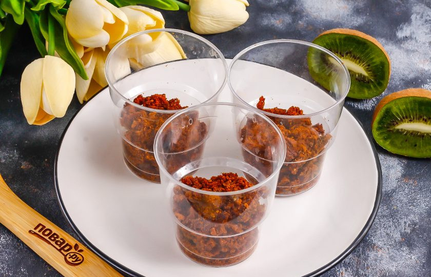 1. Этап. Трайфл с киви: В стаканы, чашки или креманки выложите песочную или бисквитную крошку. Если бисквита нет, можно измельчить обычное печенье.