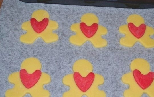 1. Этап. Простое печенье на 14 февраля: 7. Фигурки человечков разложите на противне, покрытом бумагой для выпечки. Сердечки слегка смажьте водой и прикрепите на фигурки.