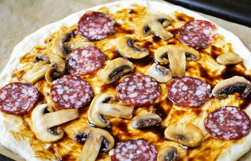 1. Этап. Пицца Терияки: Выложите кусочки копченой колбасы и жареные грибы.