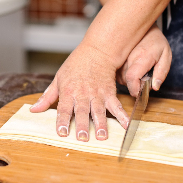 1. Этап. Норин: Как только вы достигли желаемой толщины (2 мм), сложите тесто (полоской), как показано на фотографии. Разрежьте полоску на части (по горизонтали), расстоянием от кончика большого пальца до мизинца.