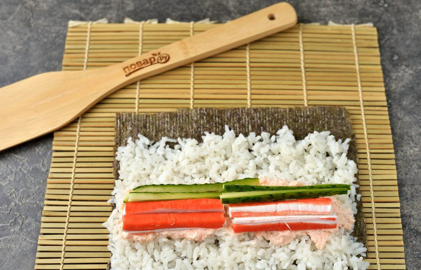 1. Этап. Роллы с икрой мойвы: Выложите на икру крабовые палочки и огурец.