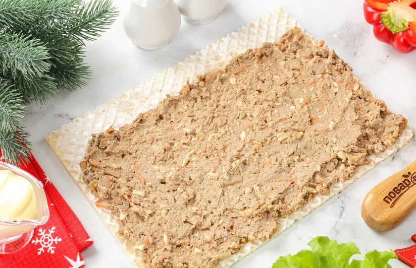 1. Этап. Рулет Новогодняя змея: Выложите на одну вафлю половину часть начинки, отступив немного от одного края и разровняйте ложкой. Накройте начинку вторым вафельным коржом и выложите оставшуюся печень.