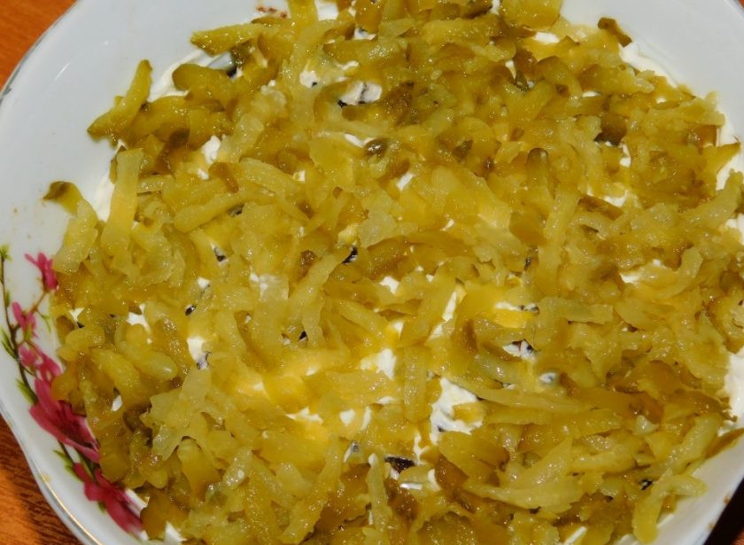 1. Этап. Слоеный салат с черносливом: Распределите слой тертых маринованных огурцов.