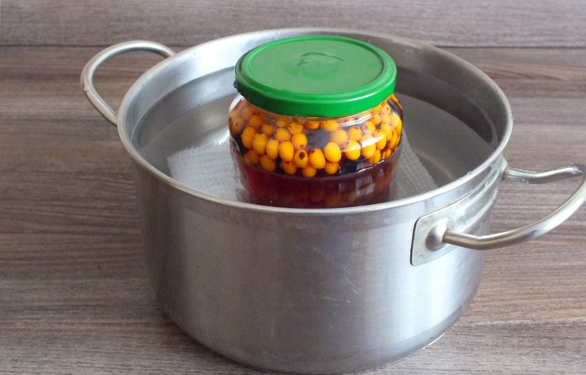 1. Этап. Компот из облепихи и черноплодной рябины: На дно просторной кастрюли выложите тканевую салфетку. Поставьте на неё банку, налейте в кастрюлю воду. Поставьте кастрюлю на огонь. С момента закипания воды, нагревайте 10 минут. После снимите с огня.