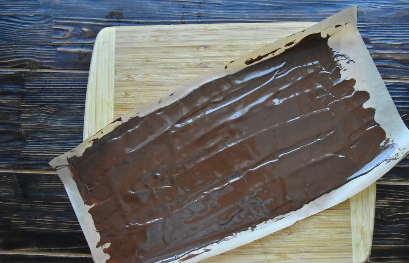 1. Этап. Торт Рождественское полено: Растопленный шоколад вылейте на пергамент и разровняйте тонким слоем. Накройт сверху вторым листом пергамента и сверните все в рулон. Поместите шоколад в морозильную камеру.