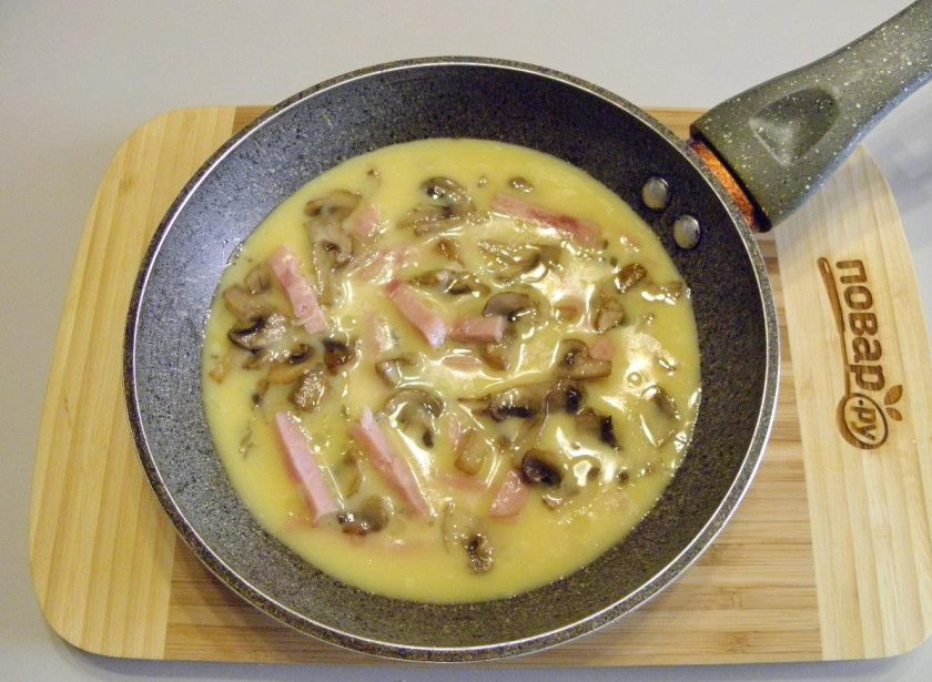 1. Этап. Омлет с ветчиной, грибами и сыром: 5. Сухую чистую сковороду смажьте щедро кусочком масла. Перелейте взбитые яйца. Сверху уложите соломки ветчины, жареные грибы.