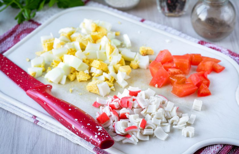 1. Этап. Салат с крабовыми палочками и чипсами: Сваренные вкрутую яйца остудите и нарежьте кубиками. Также нарежьте кубиками охлажденные крабовые палочки и свежие помидоры.