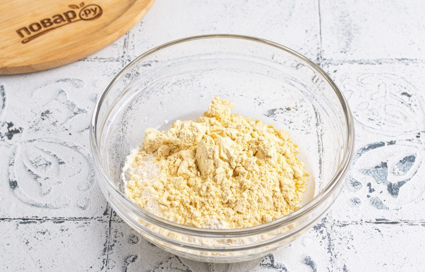 1. Этап. Печенье с изюмом из кукурузной муки: Просейте оба вида муки в миску. Перемешайте и замесите однородное тесто, которое не липнет к рукам. Если оно получается рассыпчатым, то добавьте еще пару ложек воды.