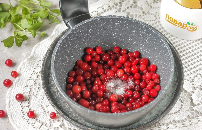 1. Этап. Медово-клюквенный конфитюр: Пересыпьте промытую клюкву в казан, ковш или в сотейник и всыпьте ванильный сахар. Поместите емкость на плиту, включая средний нагрев.