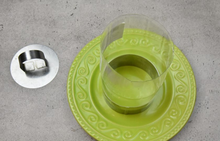 1. Этап. Пасхальный салат с консервированным лососем: Подготовьте форму для оформления слоеного салата в виде пасхального кулича и установите ее на блюдо. В данном случае используется сервировочное кольцо. Высота кольца увеличена с помощью обрезанной по краям пластиковой бутылки.