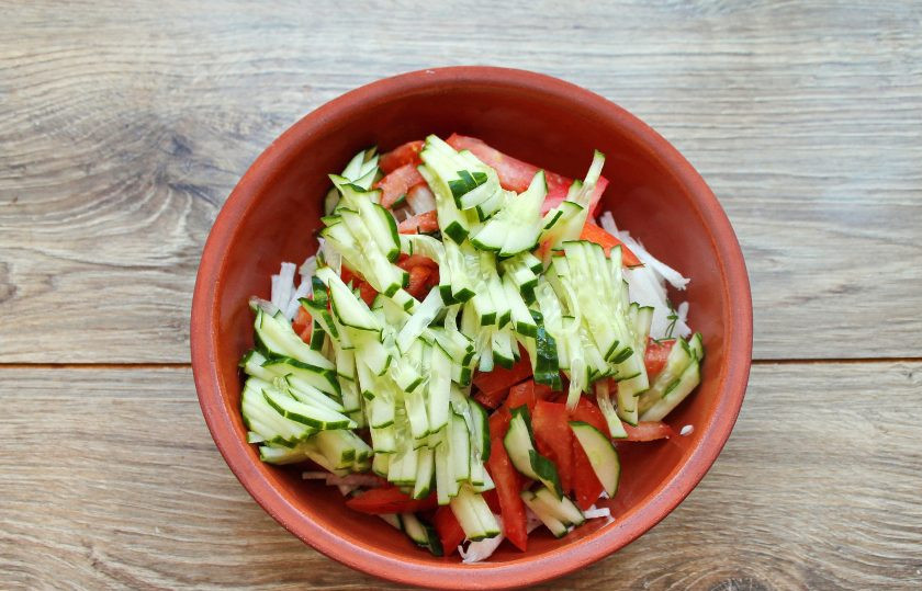 1. Этап. Салат с дайконом, огурцом и помидором: У свежего огурца отрежьте кончики и порежьте соломкой. Выложите огуречную соломку к овощам.