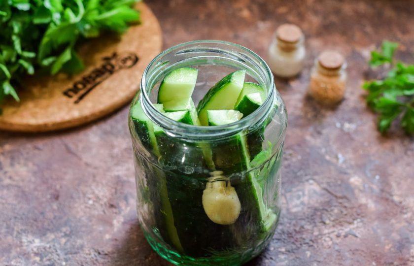 1. Этап. Ленивые огурцы на зиму: В стерильную банку выложите чистые нарезанные дольками огурцы. Добавьте укроп и чеснок.