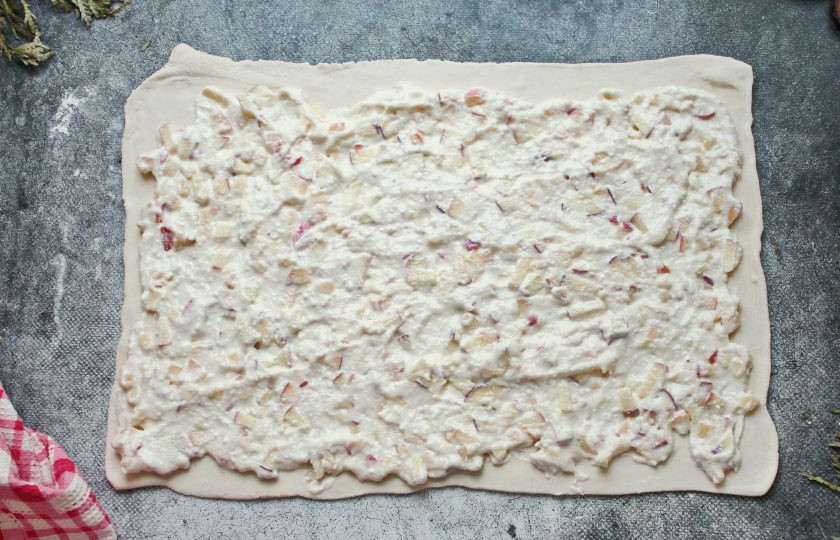 1. Этап. Булочки из слоеного теста с творогом и яблоком: Рабочую поверхность стола посыпьте мукой и выложите тесто. Слоеное тесто немного раскатайте в прямоугольник и нанесите творожную начинку с яблоками.