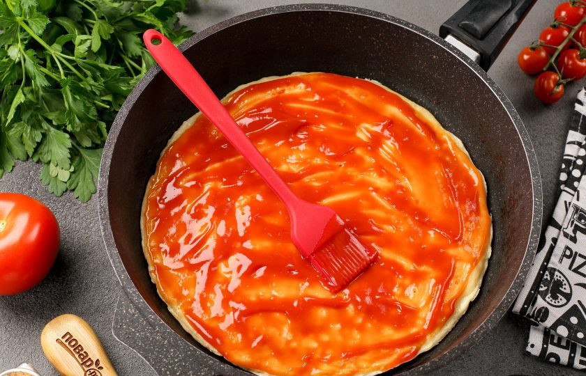 1. Этап. Пицца на сковороде без сметаны и кефира за 10 минут: При помощи силиконовой кисточки смажьте тесто томатным соусом.