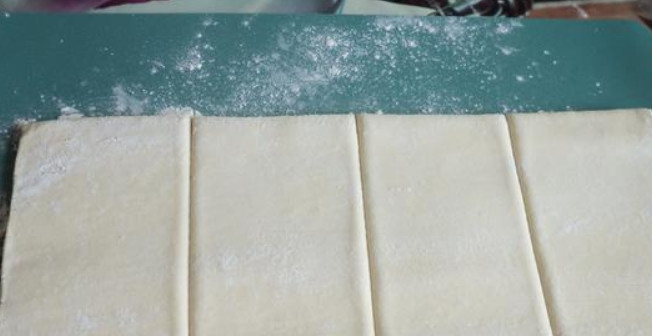 1. Этап. Слойки из готового дрожжевого теста: Размораживаем тесто, слегка раскатываем его на столе, присыпанном мукой. Разделите пласт теста на четыре прямоугольника.