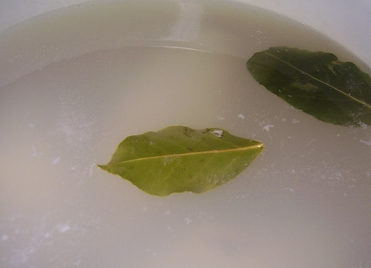 1. Этап. Салат из кальмаров с кукурузой: Закипятите воду в кастрюле, посолите ее, добавьте лавровый лист. Бросьте в нее тушки на пару минут. Затем достаньте их и очистите от пленки.