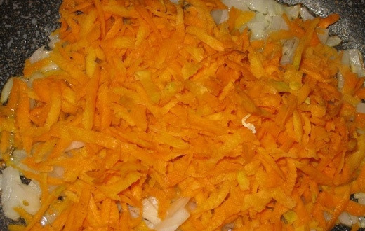 1. Этап. Суп из пельменей: Добавьте к луку натёртую морковь, которую следует предварительно промыть и очистить. Жарьте овощи вместе, помешивая.
