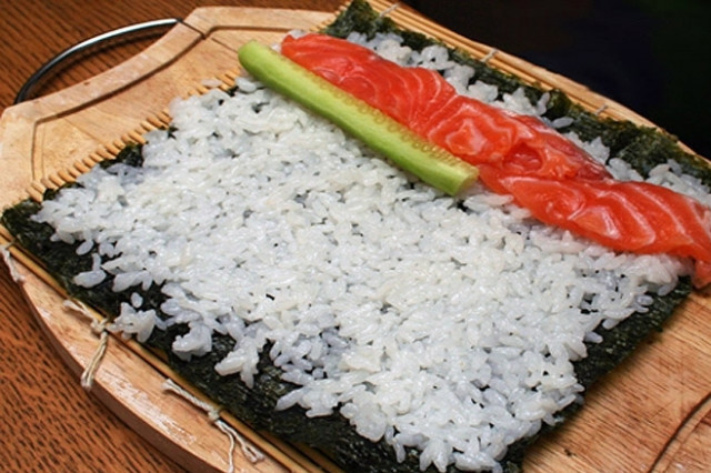 1. Этап. Суши Роллы Маки: 4. Положите на бамбуковый коврик нори. Смоченными руками положите рис слоем 3-5 мм, затем на край положите начинку: огурец с креветками, затем с тунцом и лососем.