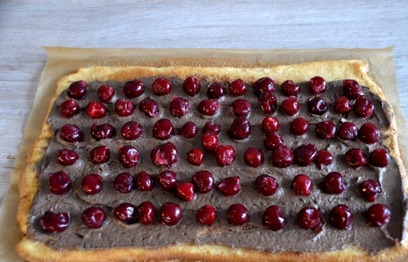 1. Этап. Торт Полено с вишней: Выложите половину крема, разровняйте, примерно 1,5-2 см. не доходя до края коржа, выложите вишню. Сверните в рулет 