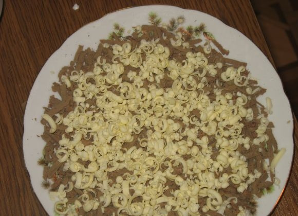 1. Этап. Новогодний печеночный торт: Выкладываем в форме круга печень на тарелку, в которой вы собираетесь подавать салат. Сверху натираем сливочное масло.