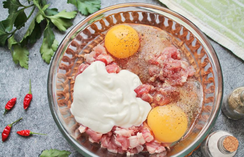 1. Этап. Мясо по-албански из свинины: Разбейте в миску со свининой яйца, выложите сметану, посолите и поперчите. Все хорошо перемешайте.
