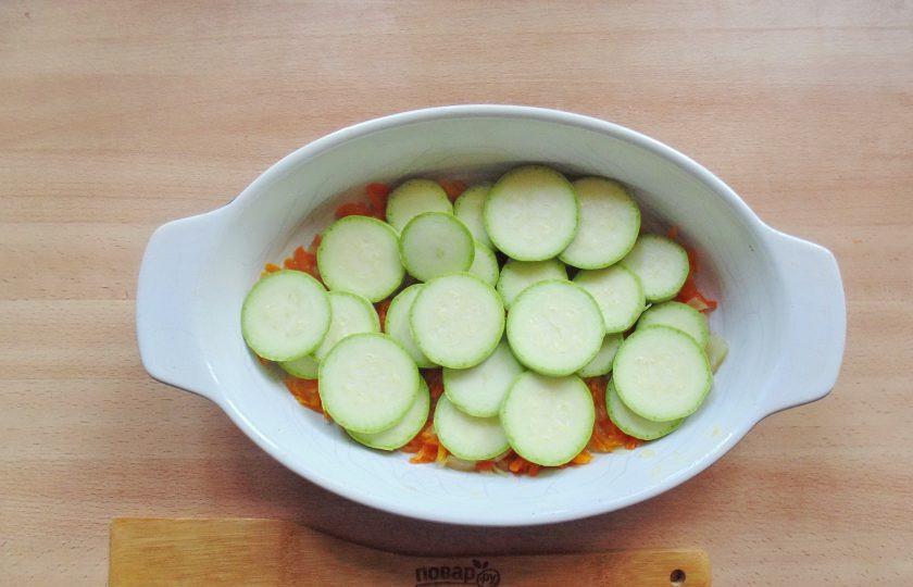 1. Этап. Хек с кабачками в духовке: Кабачки вымойте и нарежьте кружками. Выложите на морковь с луком. Немного посолите.