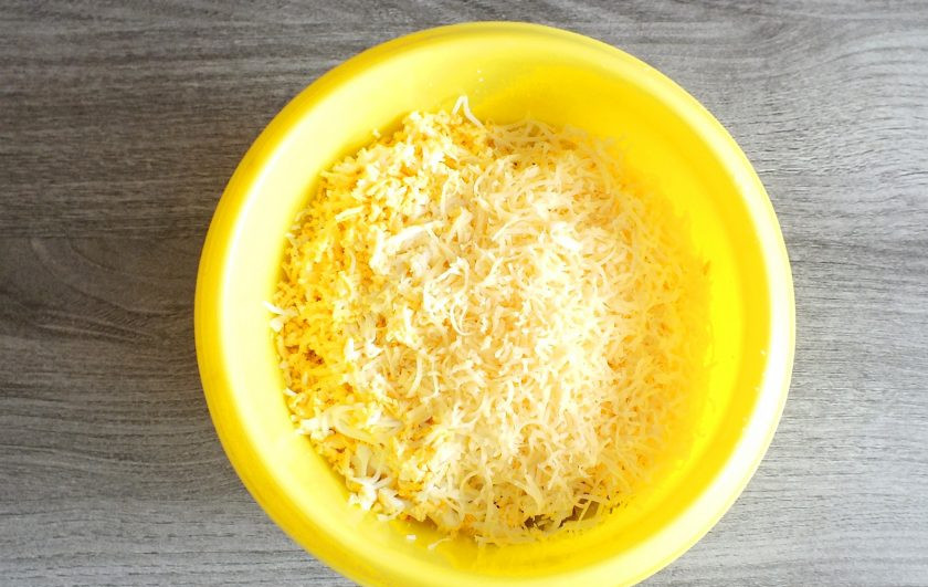 1. Этап. Крабовый салат в тарталетках: Натрите сыр на мелкой тёрке. Добавьте в чашу. Посолите по вкусу.