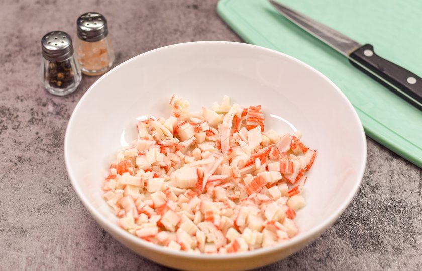 1. Этап. Закуска на чипсах на праздничный стол: Крабовые палочки нарежьте мелкими кубиками. Переложите сразу нарезку в миску.