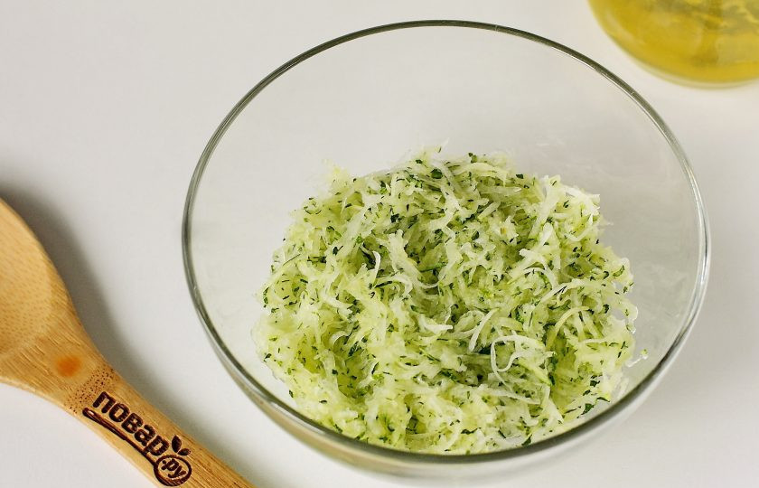 1. Этап. Оладьи из кабачков с кукурузной мукой: Кабачок натрите на терке. Можно на крупной или на мелкой, кому как больше нравится. Добавьте чайную ложку соли, помните руками и отожмите от выделившегося сока. Отжатый кабачок переложите в глубокую миску.