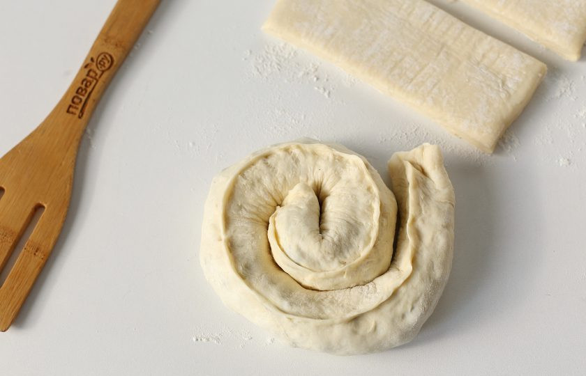 1. Этап. Слоеный пирог с мясом и грибами: Защипните тесто по всей длине и краям, а затем сверните рулетом в виде улитки.