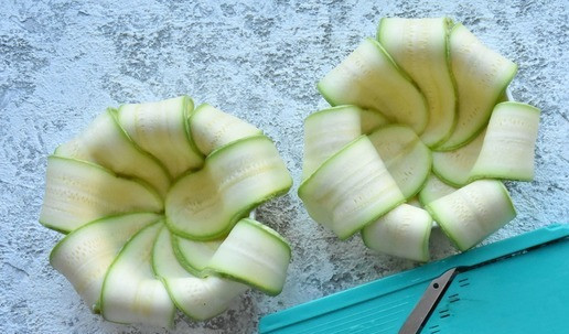 1. Этап. Нежное суфле из индейки с кабачком: Кабачок нарежьте длинными слайсами, используя овощечистку или терку мандолину. Формы для запекания смажьте сливочным маслом и выложите слайсы кабачка внахлест по кругу формы от центра дна на бока формы. Края кабачковых слайсов оставьте свободно свисающими. Формы можно использовать порционные или запечь суфле в большой форме.